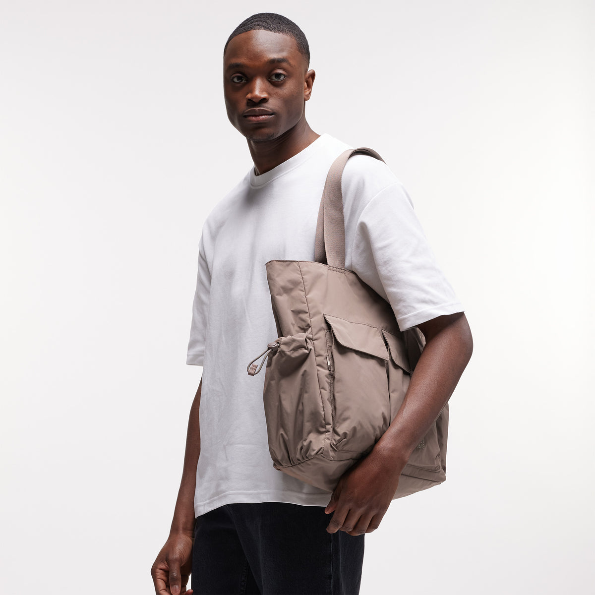 MELLOW TOTE BAG Tasche in oyster (klassisches Taupe-Braun) von einem Mann über der Schulter getragen.