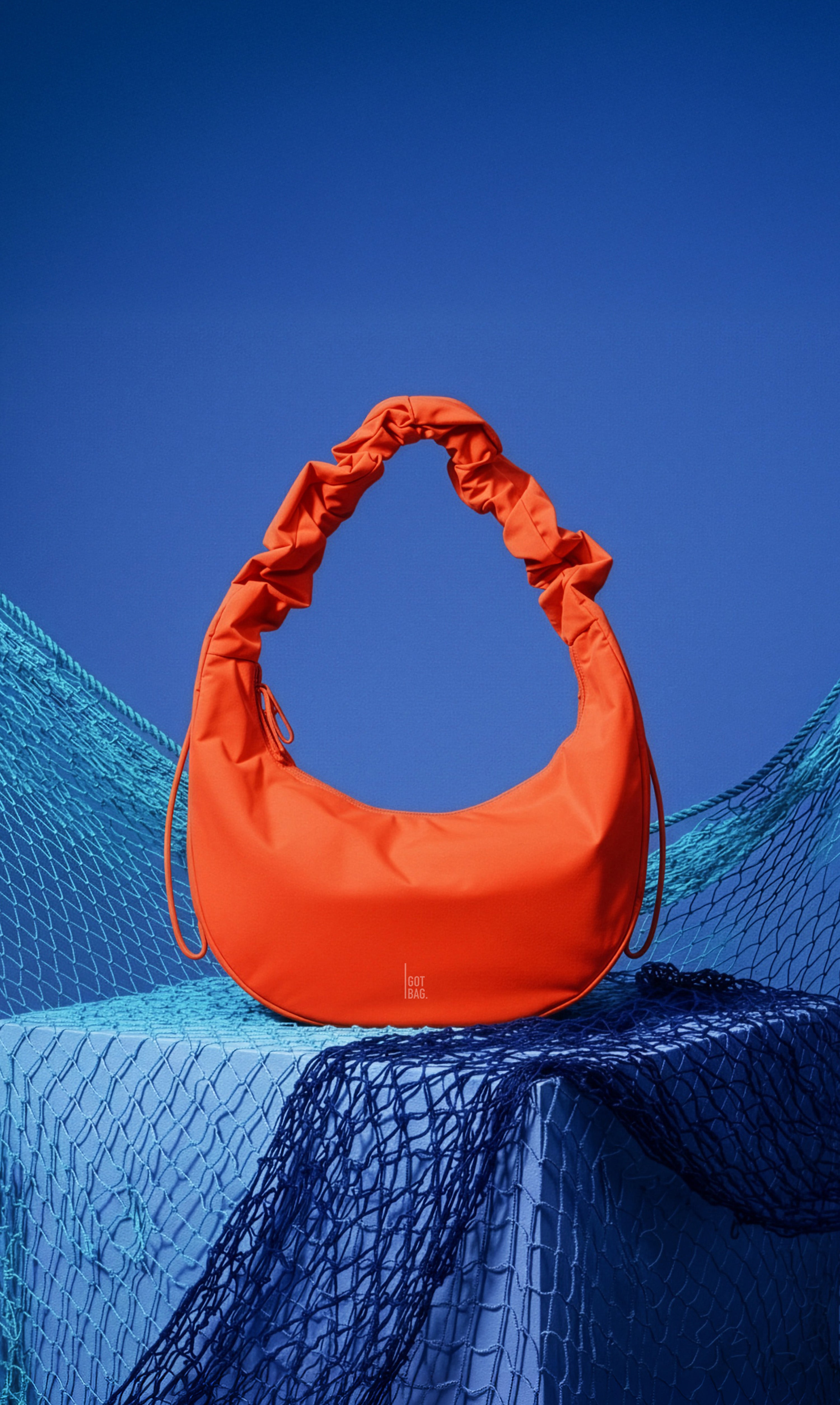 MOON BAG RUFFLE Tasche in hot coral (knalliges Orange) als Objektansicht mit Fischernetzen.