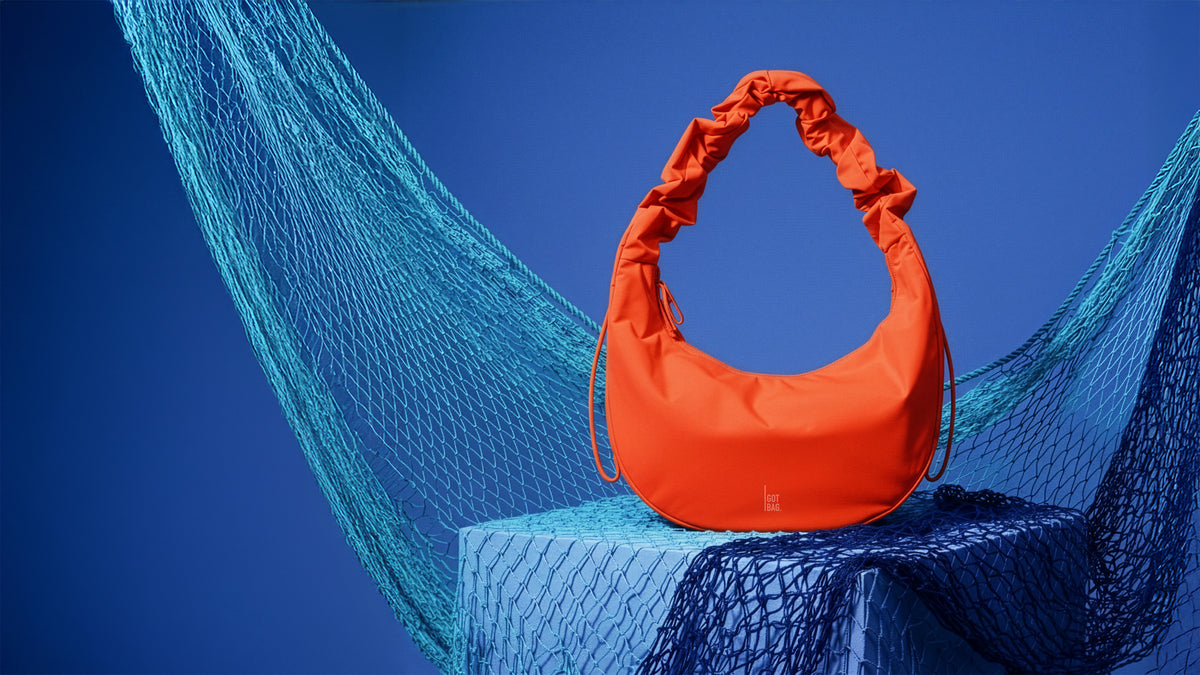 MOON BAG RUFFLE tas in hot coral (fel oranje) op een blauwe achtergrond met visnetten.