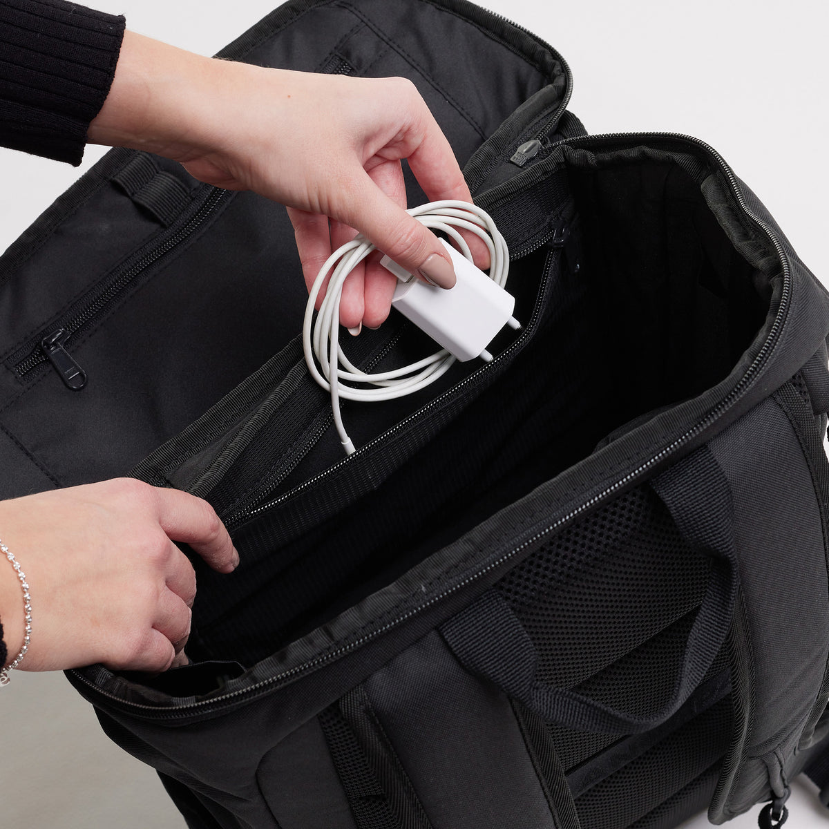 PRO PACK Rucksack in black (Schwarz), eine Frau verstaut ein Ladekabel in einer Innentasche.