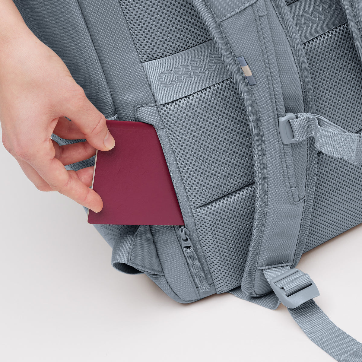 PRO PACK Rucksack in marlin (grau-blau), eine Hand steckt einen Pass in eine versteckte Tasche.