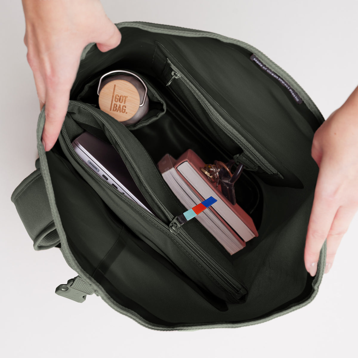 ROLLTOP Rucksack in algae (Dunkelgrün mit Graustich), von einer Frau geöffnet, Innenansicht mit Flasche, Laptop und Notizbüchern.