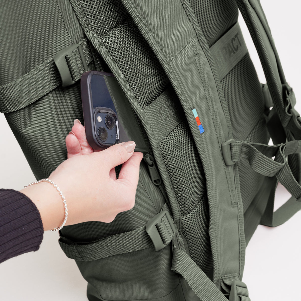 ROLLTOP Rucksack in algae (Dunkelgrün mit Graustich) von einer Frau, die ein Smartphone in eine Reißverschlusstasche steckt.