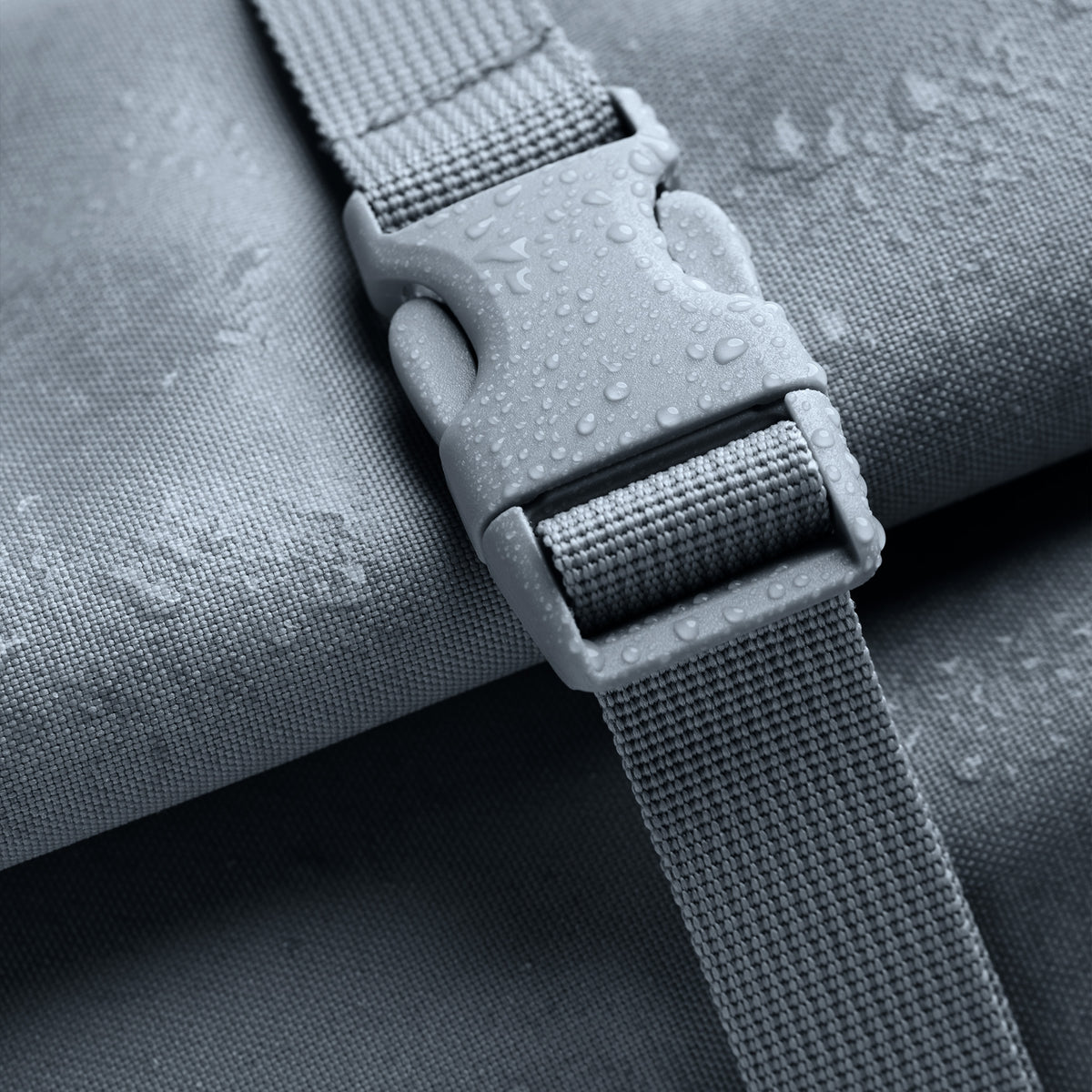 Detailaufnahme des ROLLTOP LITE Rucksacks in marlin (grau-blau) mit Wassertropfen auf Schnalle und Stoff.