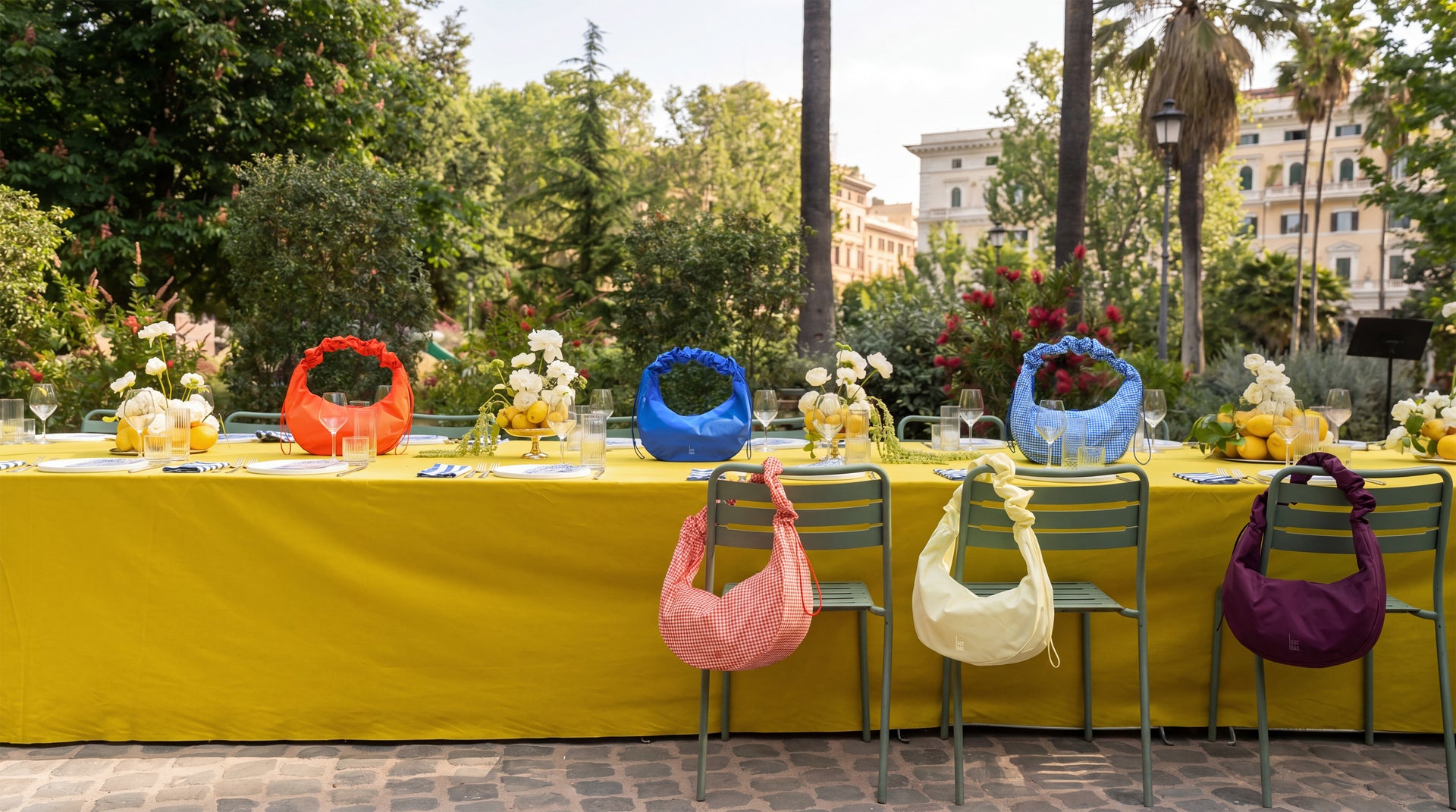 Vier RUFFLE HAPPENING HP Taschen in verschiedenen Farben auf und an einem Esstisch im Freien.