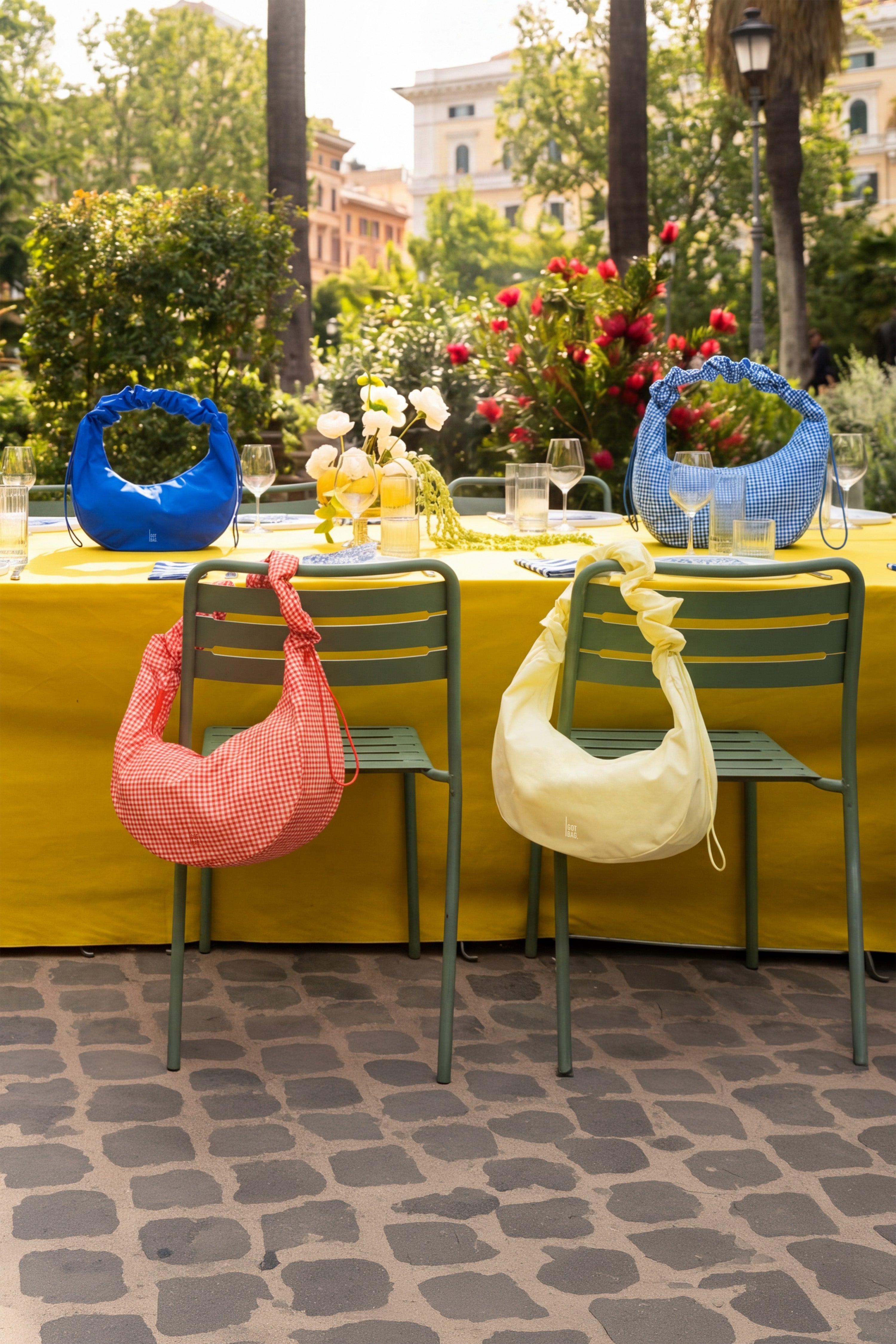 Vier RUFFLE HAPPENING HP Taschen in verschiedenen Farben auf und an einem Esstisch im Freien.