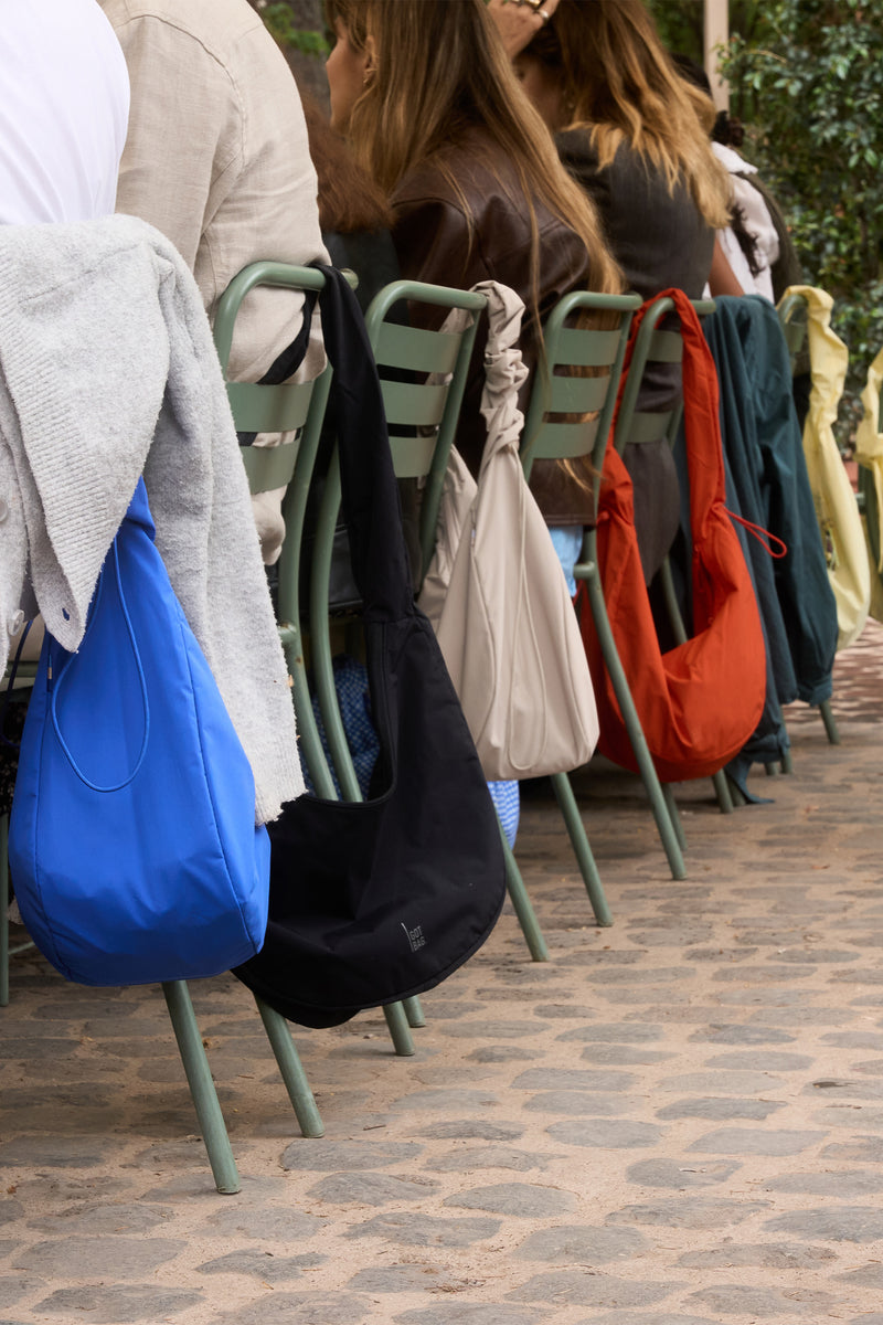 Meerdere tassen hangen aan de rugleuningen van stoelen, waaraan gasten buiten zitten.