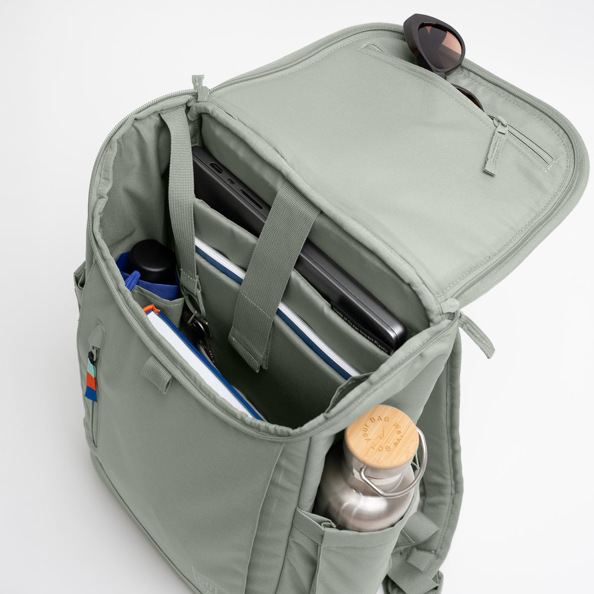 SERENE PACK Rucksack in bass (Salbeigrün) offen, mit Laptop, Schlüsseln und Wasserflasche, Innenansicht.