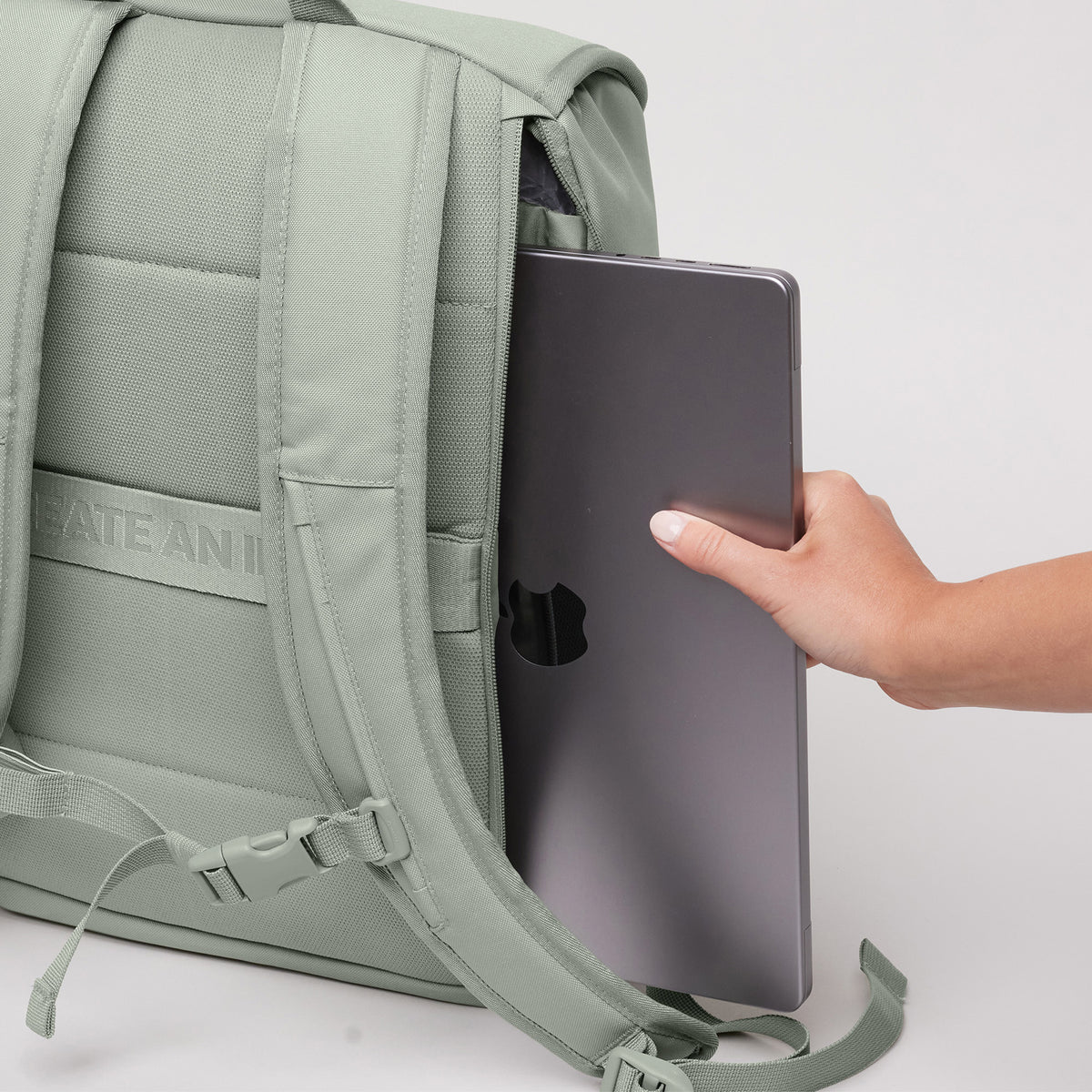 SERENE PACK Rucksack in bass (Salbeigrün) von einer Frau, die einen Laptop in das Reißverschlussfach steckt.