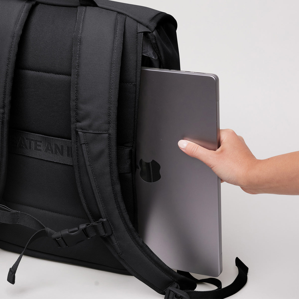 SERENE PACK Rucksack in black (Schwarz), eine Hand schiebt einen Laptop in die Seitentasche.