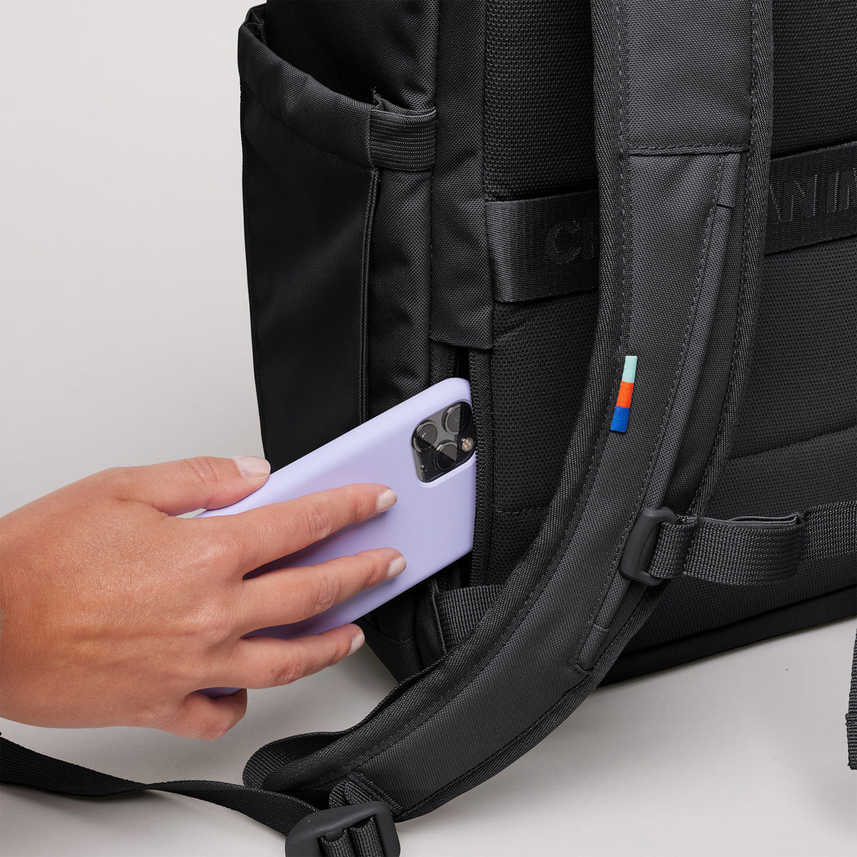 SERENE PACK Rucksack in black (Schwarz) mit einer Hand, die ein Handy in die Seitentasche legt.
