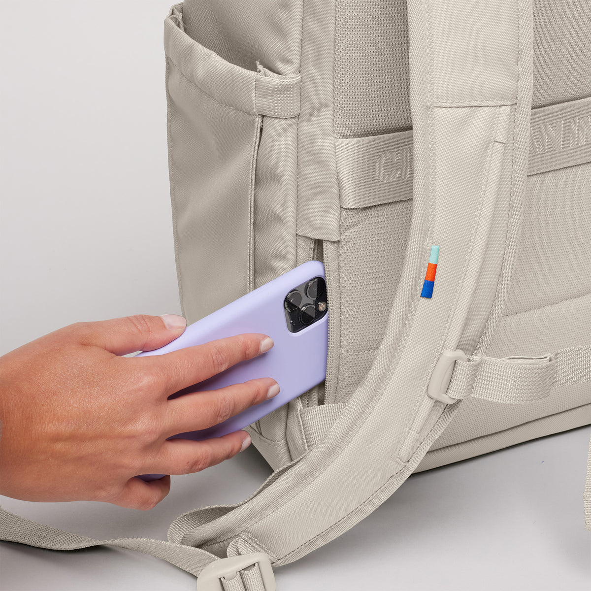 SERENE PACK Rucksack in soft shell (warmes Cremeweiß). Frau steckt Smartphone in Seitentasche.