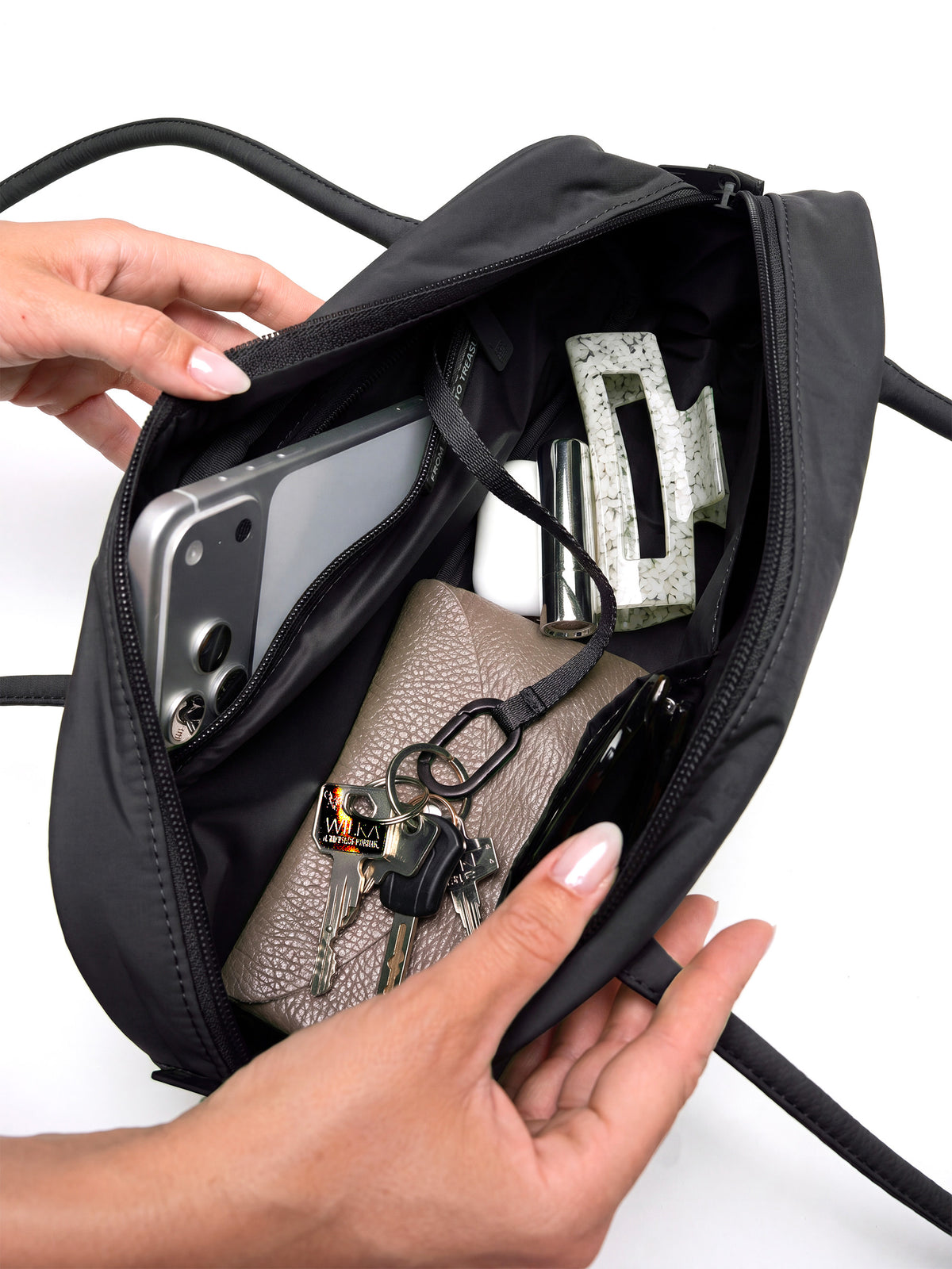 STRIKE BAG SMALL Tasche in black (Schwarz) von Händen geöffnet, zeigt Smartphone, Schlüssel und weitere Gegenstände im Inneren.
