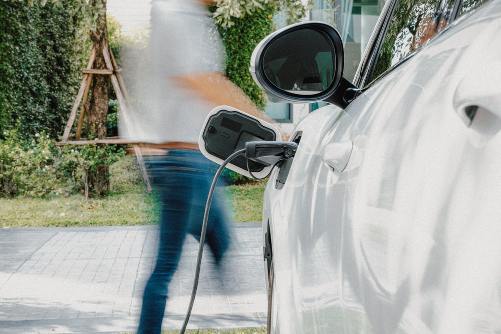 Uomo ricarica un'auto elettrica bianca a casa. La scena mostra accessori.