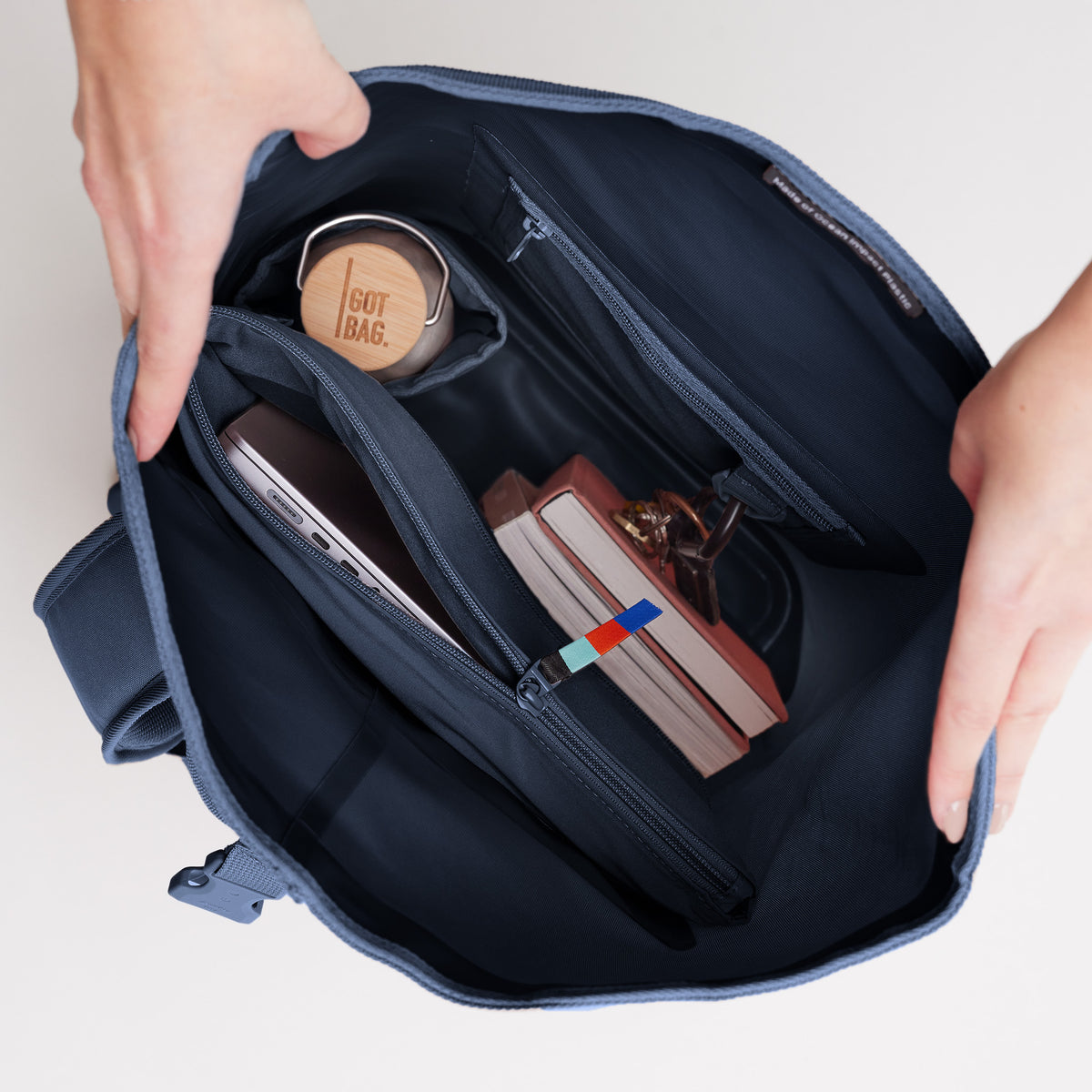 Innenansicht eines Rucksacks, von Händen offen gehalten, zeigt Laptop, Flasche und Notizbuch.