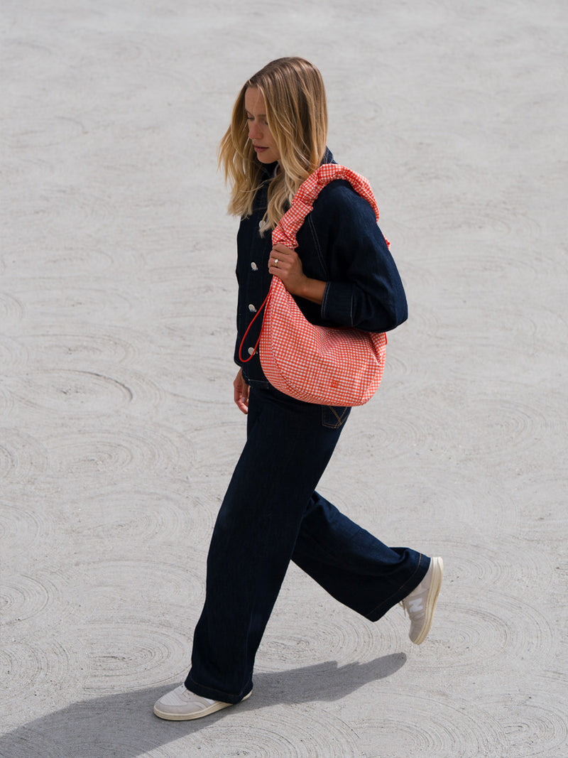 MOON BAG RUFFLE tas in vichy hot coral (Oranje-beige geruit) over de schouder gedragen door een vrouw.