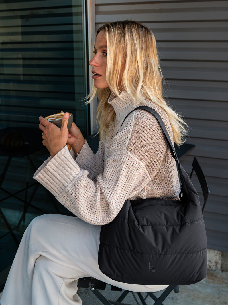 PUFFER SQUARE BAG Tasche in black (Schwarz) von einer Frau über der Schulter getragen.