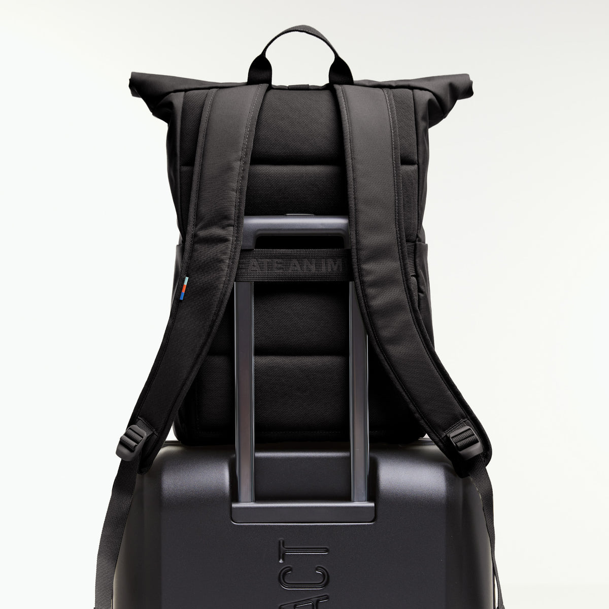 Rucksack auf einem Koffer mit durchgeschobenem Teleskopgriff, zeigt die Rückansicht und ein farbiges Etikett.