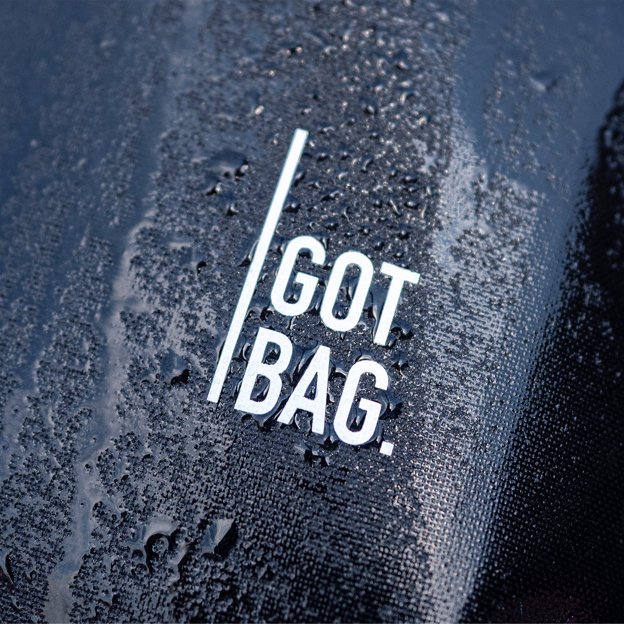 Detailaufnahme einer GOT BAG Tasche mit Logo und glänzenden Wassertropfen auf der strukturierten Oberfläche.