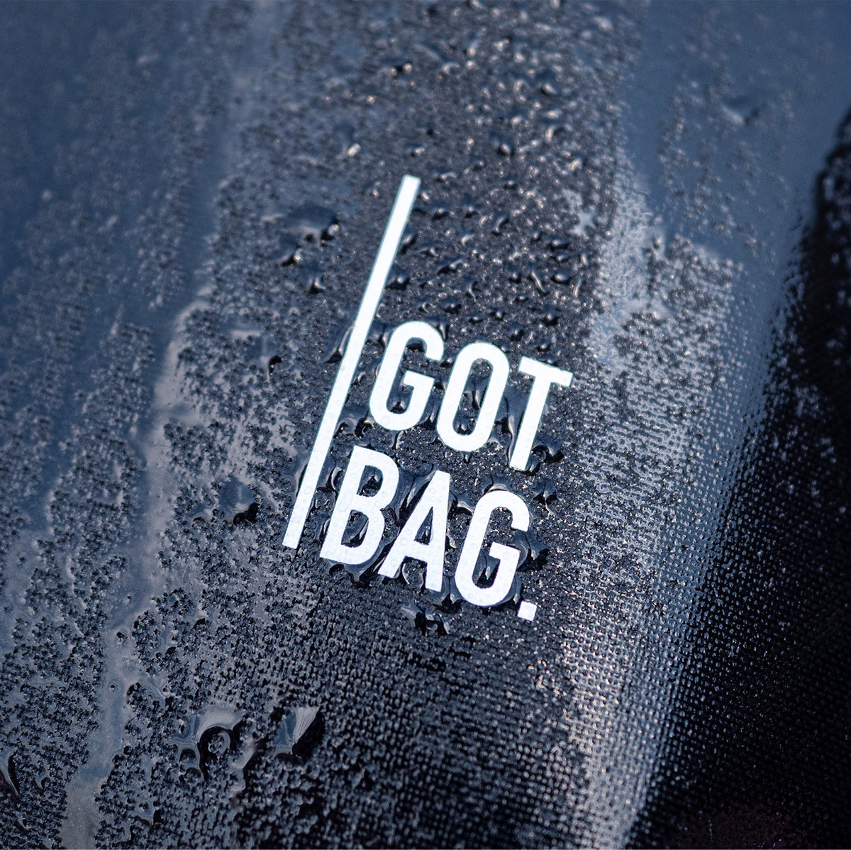 Detailaufnahme einer GOT BAG Tasche mit Logo und glänzenden Wassertropfen auf der strukturierten Oberfläche.