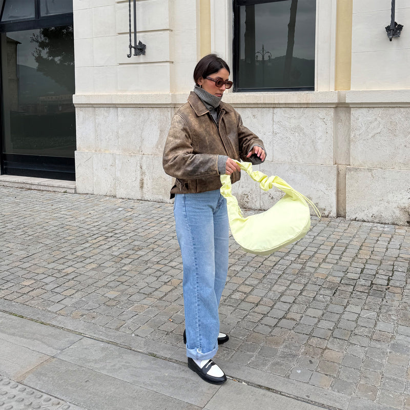 MOON BAG RUFFLE tas in sea lemon (zacht pastelgeel) in de hand gehouden door een vrouw.