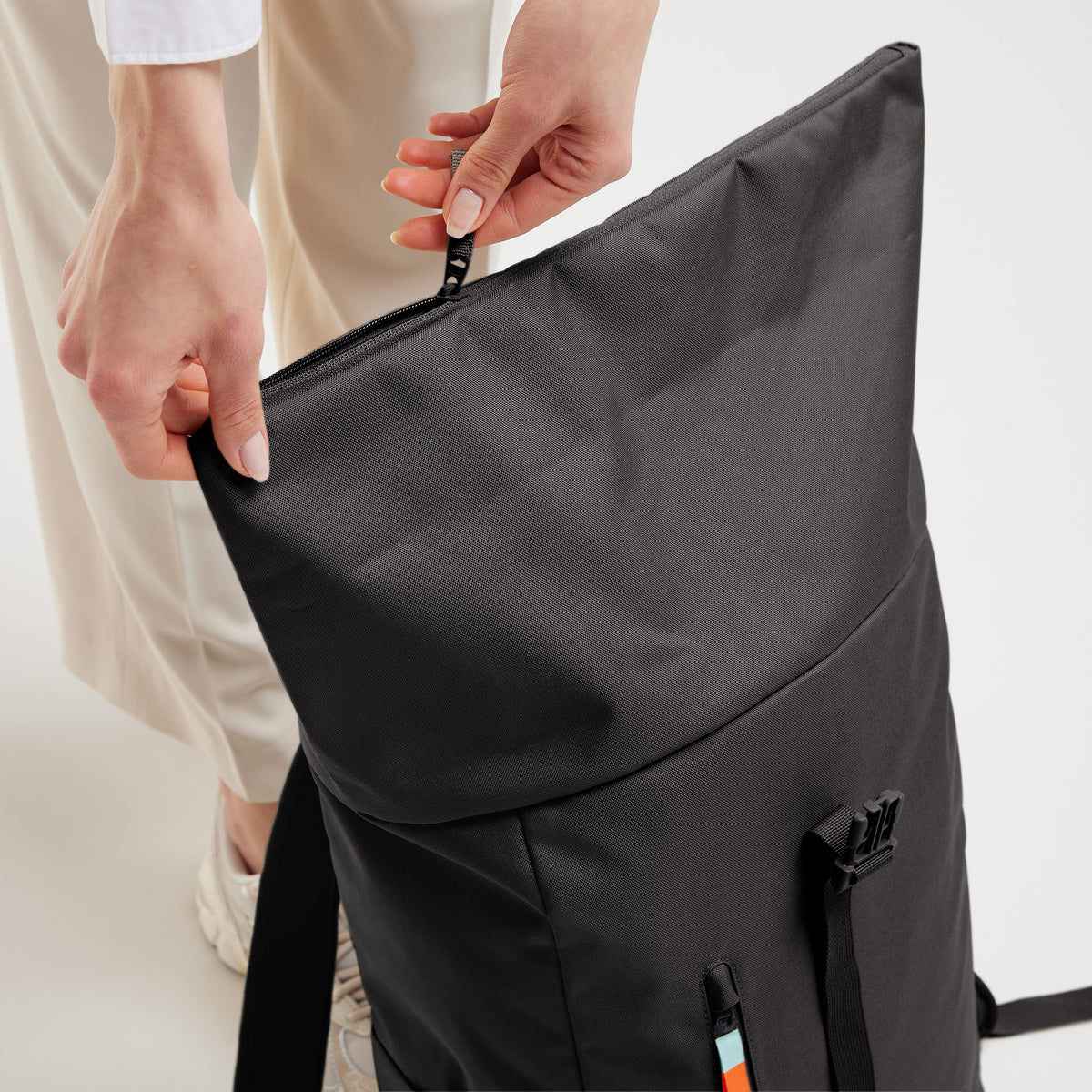Eine Frau öffnet den Reißverschluss eines Rolltop Rucksacks.
