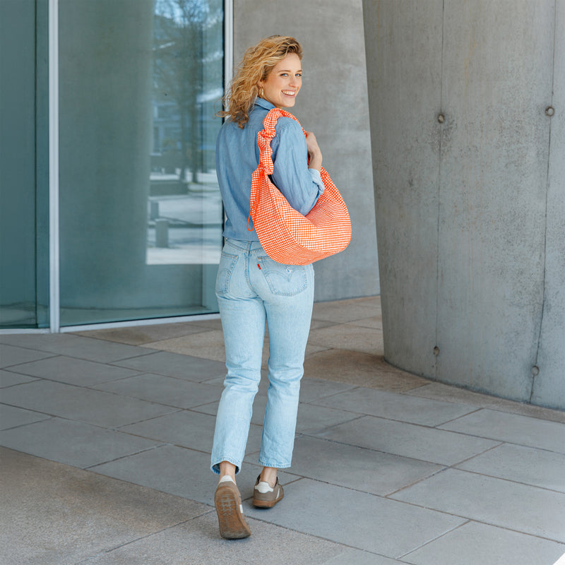 MOON BAG RUFFLE tas in vichy hot coral (Oranje-beige geruit) gedragen over de schouder door een vrouw.
