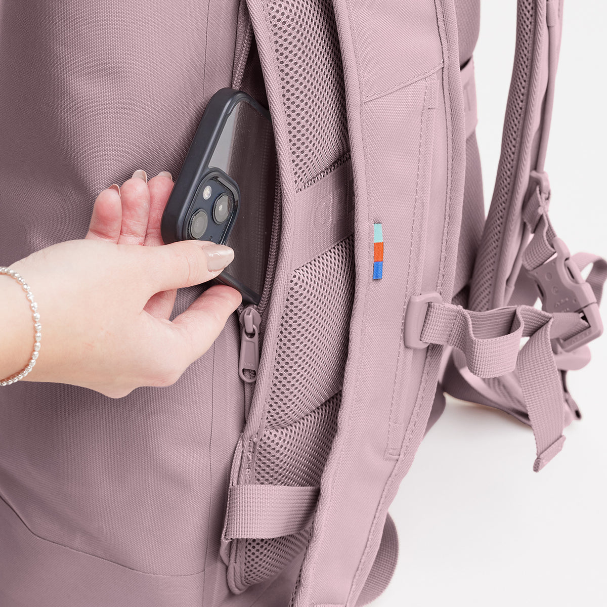 Detailaufnahme eines Rucksacks, in dessen seitliche Geheimtasche eine Frau ein Smartphone steckt.