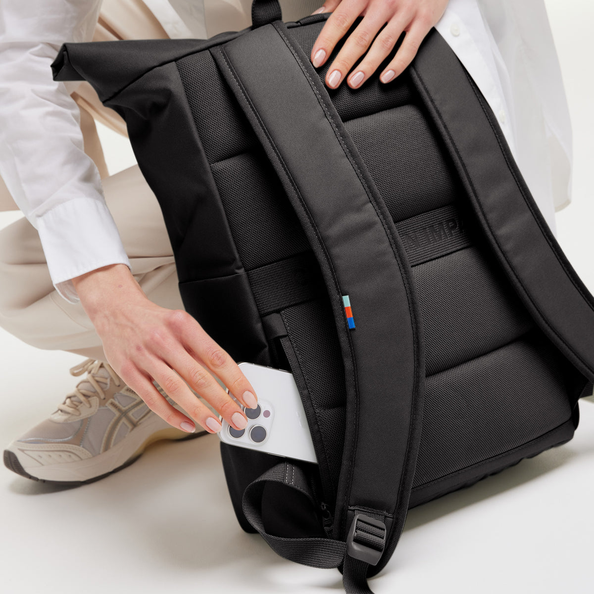 Rucksack mit secret pocket an der Rückseite, in den eine Frau ein weißes Smartphone steckt.