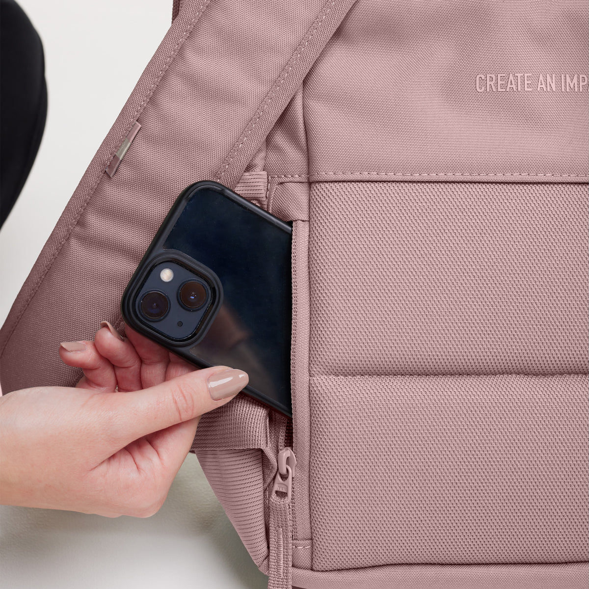 Detailaufnahme eines Rucksacks: eine Frau steckt ein Smartphone in ein Geheimfach.