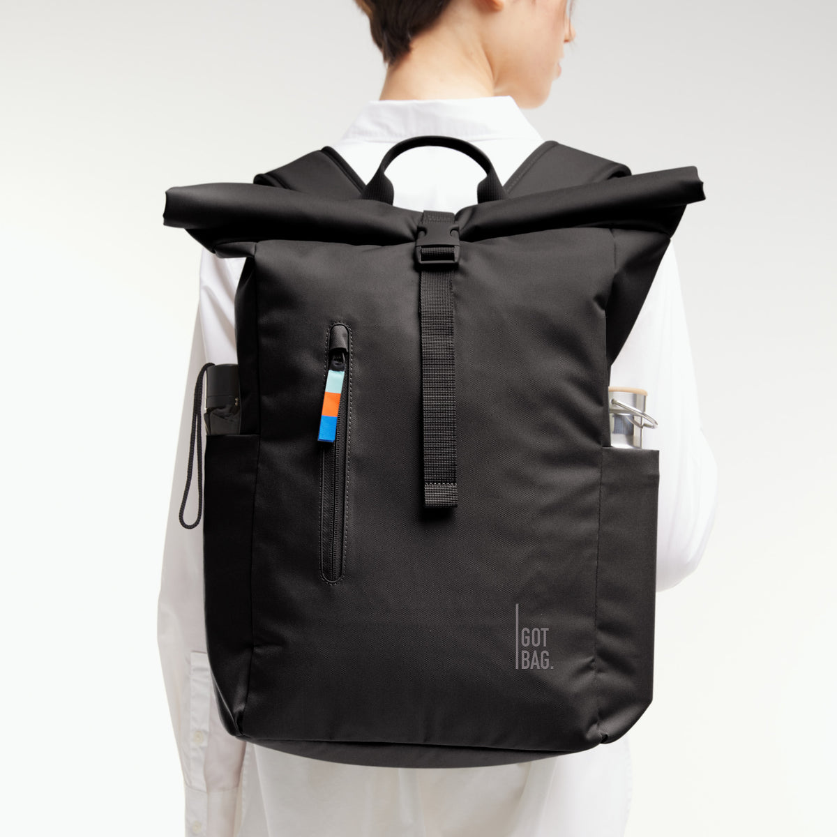 Rucksack, von einer Frau auf dem Rücken getragen, mit Rolltop-Verschluss, seitlichen Fächern und Reißverschlusstasche.
