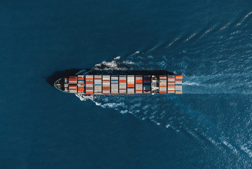 Vista aerea di una nave portacontainer, carica di container colorati, su un mare blu scuro.