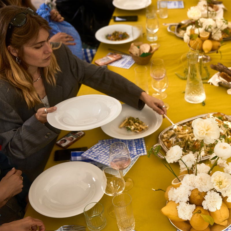 Accessoires, gepresenteerd door een vrouw die gerechten aan een gedekte tafel serveert.