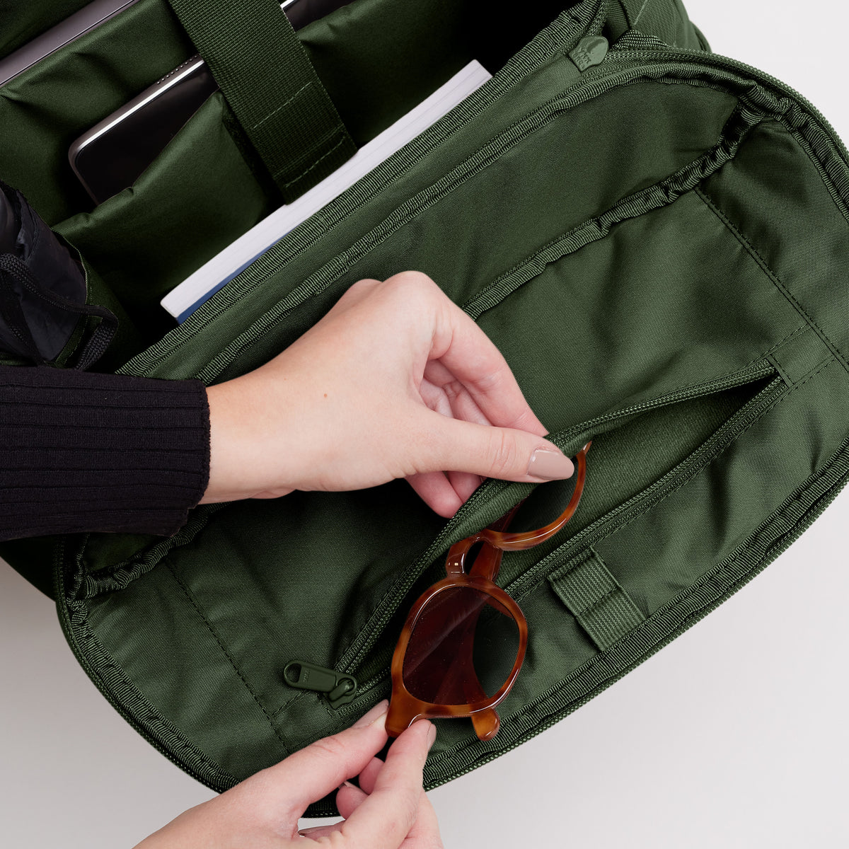 Eine Frau steckt eine Sonnenbrille in die Reißverschlusstasche einer Tasche.