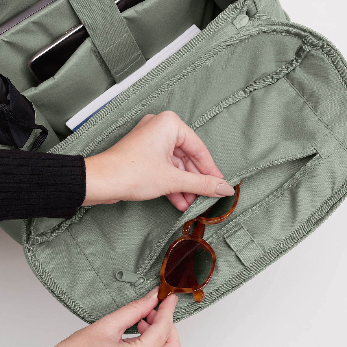 Detailaufnahme einer Sonnenbrille (Accessoires), von Händen in die Reißverschlusstasche einer Tasche gesteckt.